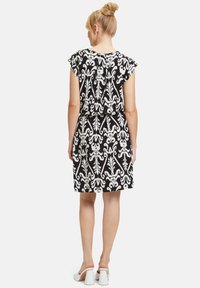 Schwarzes und weißes gemustertes Kleid mit kurzen, schwingenden Ärmeln, lockerer Passform, einer Länge bis über das Knie und einem dezenten Blumenmuster.