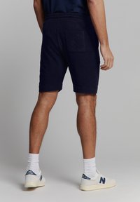 Marineblauwe katoenen shorts met een elastische tailleband, voorzien van een achterzak en een casual snit, in combinatie met witte sokken en sneakers.
