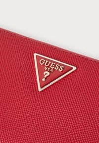 Red textured wallet featuring a triangular gold and red logo with "GUESS USA" and a question mark detail.