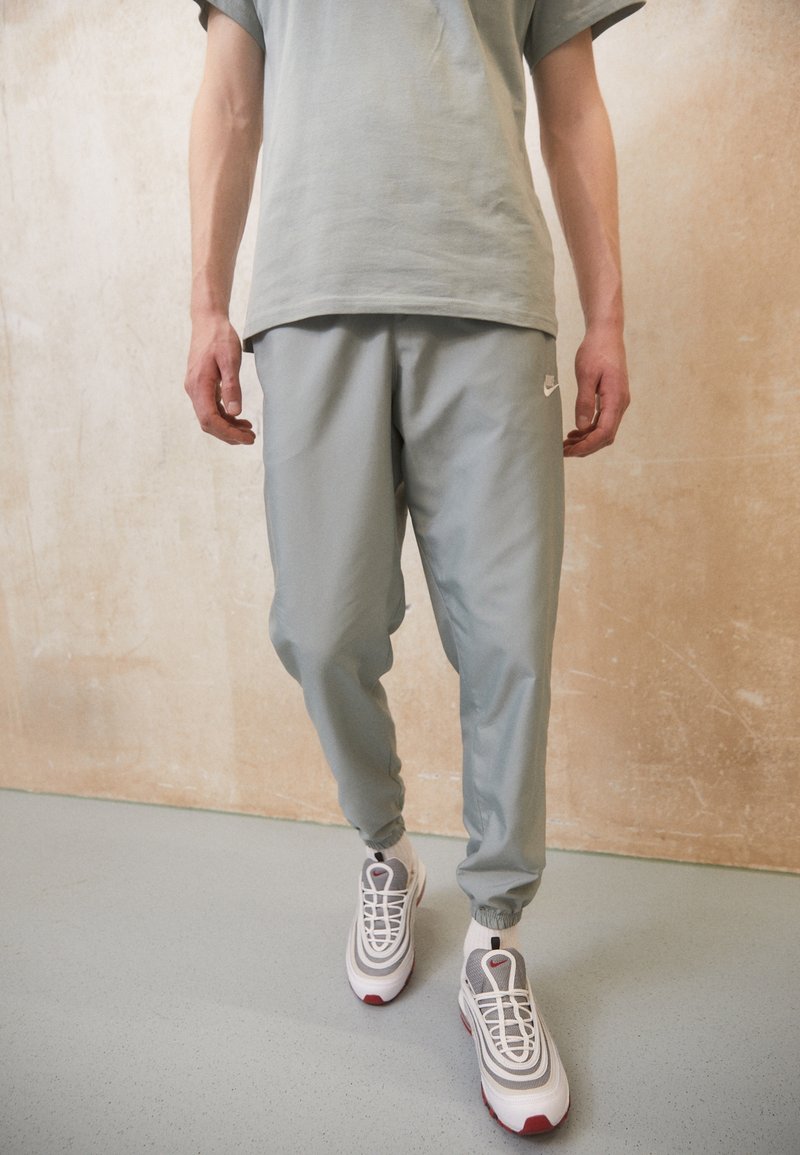 Ljust grå träningsbyxor med elastiska muddarna och midjan, i kombination med vita och grå sneakers med röda detaljer. Minimalistisk design.