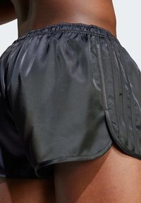 Schwarze Sportshorts aus glänzendem, glattem Material. Mit einem weichen, elastischen Bund und seitlichen Streifen als Designelement.