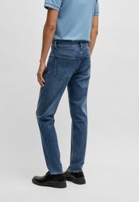 Dark blue denim jeans with a straight cut, featuring five pockets and classic stitching details. Paired with black lace-up shoes.