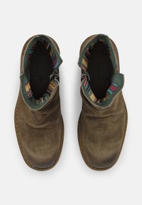 Bottines en suede marron avec une finition texturée, dotées d'un col en cuir vert et d'une doublure intérieure à motif dans différentes couleurs.