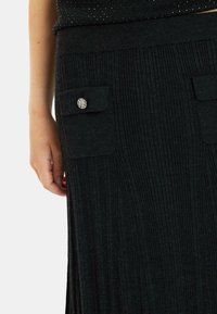 Gonna nera a costine con tessuto texturizzato, caratterizzata da due tasche frontali e bottoni decorativi in argento sui pattini delle tasche.
