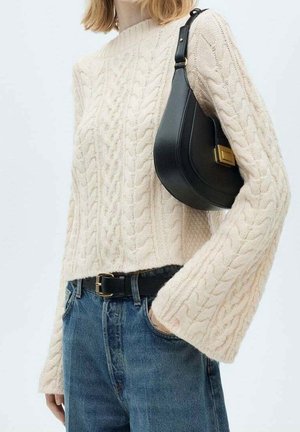 Kvinde iført cremefarvet kabelstrikket sweater og blå jeans med sort bælte, bærende en sort læder skuldertaske med guldspænde.