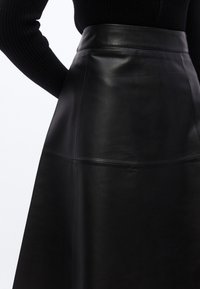 Μαύρη δερμάτινη φούστα με λείο υφή, ψηλή μέση και ραφές σε πάνελ. Κομμένη σε φαρδιά σιλουέτα για κλασική εμφάνιση.