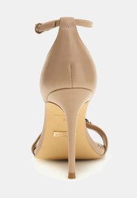 Beige korkokengät avonaisella varrella, ohuella stiletto-korolla ja sileällä nahkapinnalla esitellen takaapäin valkoista taustaa vasten.