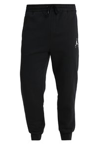 Černé tepláky vyrobené z měkké látky s elastickým pasem, stahovací šňůrkou, užšími nohavicemi a malou bílou značkou na levém stehně.