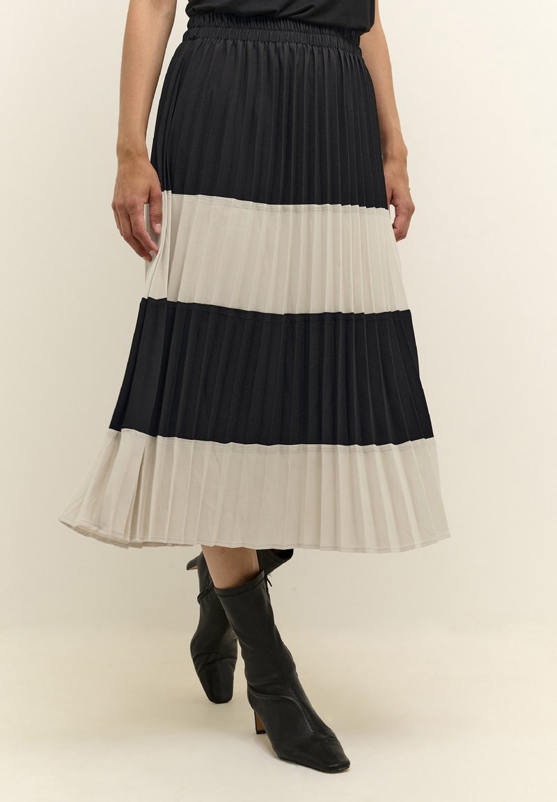 Skládaná sukně s černými a béžovými vodorovnými pruhy, elastickým pasem, volným střihem a délkou do poloviny lýtek. Nošena s černými kotníkovými botami.