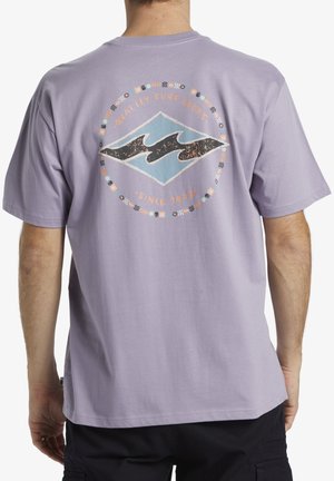T-shirt en coton violet avec un graphique au dos représentant un logo bleu et noir, entouré d'un motif floral circulaire et du texte "Qualité Assurée depuis 1993."