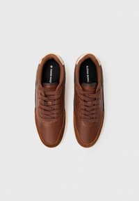 Braune Ledersneaker mit glatter Oberfläche, strukturierten Akzenten und durchbrochenen Details an der Zehe. Ausgestattet mit braunen Schnürsenkeln und Logo.