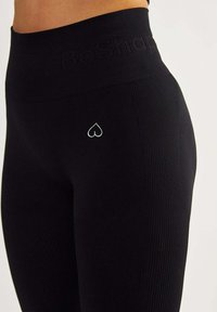 Black ribbed leggings with a high waistband featuring embossed text and a small white heart logo on the side. Elastic material ensures comfort.
