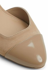 Beige high-heeled shoe featuring a suede upper, cut-out design, and a glossy patent leather pointed toe. Smooth texture with sleek lines.
