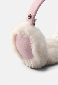 Rosa mockasinfodral med mjukt vitt pälsfoder. Inkluderar en märkesknapp i metall. Kuddens textur verkar varm och inbjudande.