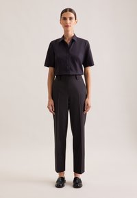 Czarna, krótka koszula na guziki z kołnierzykiem, zestawiona z wysokim stanem czarnych, dopasowanych spodni oraz czarnych mokasynów. Prosty, przemyślany design.