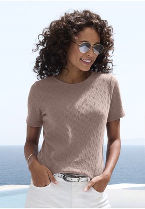 Hellbraunes, gestricktes T-Shirt mit geometrischem Muster, kurzen Ärmeln und Rundhalsausschnitt, kombiniert mit weißen, hochgeschnittenen Hosen und einem Gürtel.