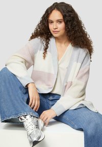 Leichter, mehrfarbiger Cardigan mit vertikalen Streifen in pastellrosa, blau und weiß. Verfügt über einen offenen Front und weite Ärmel, getragen über einem cremefarbenen Top.