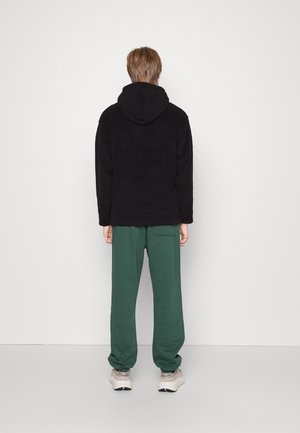 Sort fleece hoodie med snoretræk i hætten, parret med løstsiddende grønne sweatpants med en sidelomme, båret med beige sneakers.
