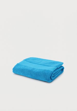 Serviette bleue vif pliée avec une bande texturée, placée sur un fond blanc uni.
