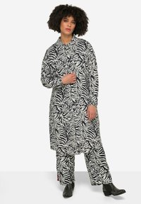 Schwarzes und weißes Zebra-Print Hemdkleid mit langen Ärmeln, Knopfleiste und passender Hose. Hat eine lockere Passform und ist aus einem weichen Textil gefertigt.