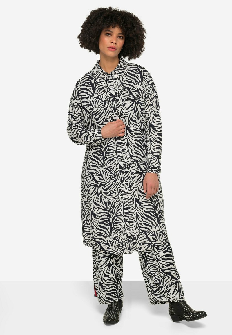 Schwarzes und weißes Zebra-Print Hemdkleid mit langen Ärmeln, Knopfleiste und passender Hose. Hat eine lockere Passform und ist aus einem weichen Textil gefertigt.