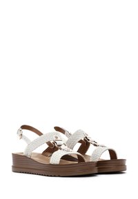 Witte geweven sandalen met verstelbare banden, gouden hardware accenten en een bruine platformzool met een gestructureerde grip.