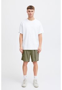 White cotton t-shirt with short sleeves, paired with green shorts in a textured fabric. Footwear is light grey sneakers. Clean, minimal design.