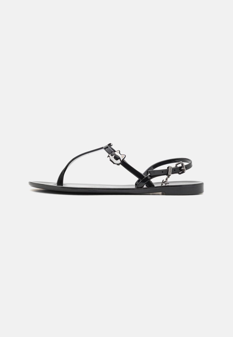 Sandalias planas pretas com um design minimalista, apresentando tiras finas e detalhes decorativos em metal. Feitas de um material suave e brilhante.