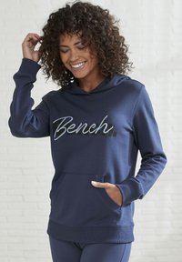 Navyblauer Hoodie mit einer Fronttasche, auf der das Wort "Bench." in einer Mischung aus schwarzer und silberner Schrift steht. Weicher Stoff und gerippte Bündchen.