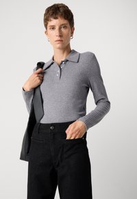 Camisa polo de manga larga color gris con ribetes, con cuello clásico y cierre de botones, combinada con pantalones negros de cintura alta que presentan sutiles destellos.