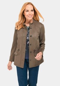 Braune Wildlederjacke mit Mandarin-Kragen, Fronttaschen und Knopfverschlüssen. Kombiniert mit einem blauen Blümchenoberteil und dunklen Jeans.