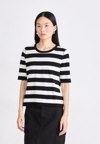 Zwart-witte gestreepte korte mouwen shirt van zacht materiaal met een ronde hals. Heeft een klein logo accent aan de zoom.