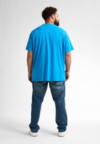 Tricou din bumbac albastru deschis cu guler rotund, asortat cu blugi albaștri decolorati. Croiala este lejeră, iar materialul pare neted și ușor.