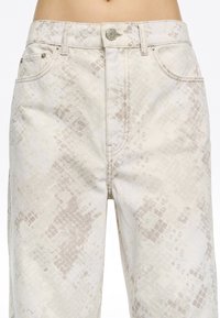 Jean beige avec un motif serpent discret ; confectionné en denim, doté d'une fermeture à bouton en métal et de poches avant.