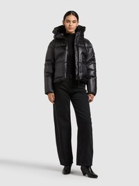 Zwarte gewatteerde jas met ritssluiting en capuchon, voorzien van doorgestikte vulling en een glanzende afwerking, gecombineerd met zwarte wijd uitlopende jeans en enkellaarsjes.