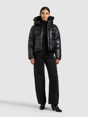 Veste matelassée noire avec fermeture éclair et capuche, dotée d'un rembourrage matelassé et d'une finition brillante, associée à un jean noir à jambes larges et des bottines.