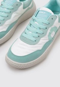 Baskets bleu clair et blanches avec un dessus en daim texturé et toile, bout arrondi, semelle en caoutchouc, et un détail logo en forme de cœur sur le côté.