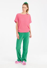 Top corto rosa a righe con maniche corte, pantaloni verdi morbidi e testurizzati, e sandali a scivolo rosa. Design semplice e casual con vestibilità rilassata e colori vivaci.