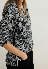 Black and gray patterned long-sleeve shirt with a V-neckline, featuring contrasting side stripes and a relaxed fit.