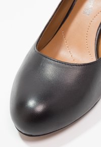 Chaussure plate pour femme en cuir noir à bout arrondi avec semelle intérieure beige cousue visible à l'intérieur.