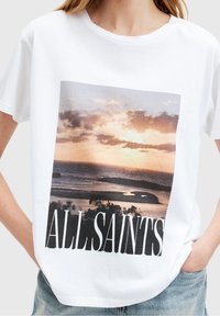 Bílý bavlněný tričko s velkým grafickým motivem západu slunce a textem "ALL SAINTS" v černé barvě, s krátkými rukávy a volným střihem.