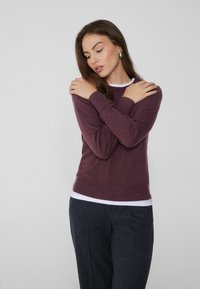 Burgundowy sweter z dzianiny z okrągłym dekoltem, ściągaczami przy rękawach i u dołu, nałożony na białą koszulę, zestawiony z ciemnoszarymi spodniami. Gładka tekstura, dopasowany krój.