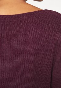 Stickad tröja i djup burgunder med en strukturerad, ribbad design. Den har en vid halsringning och korta ärmar för en avslappnad passform.