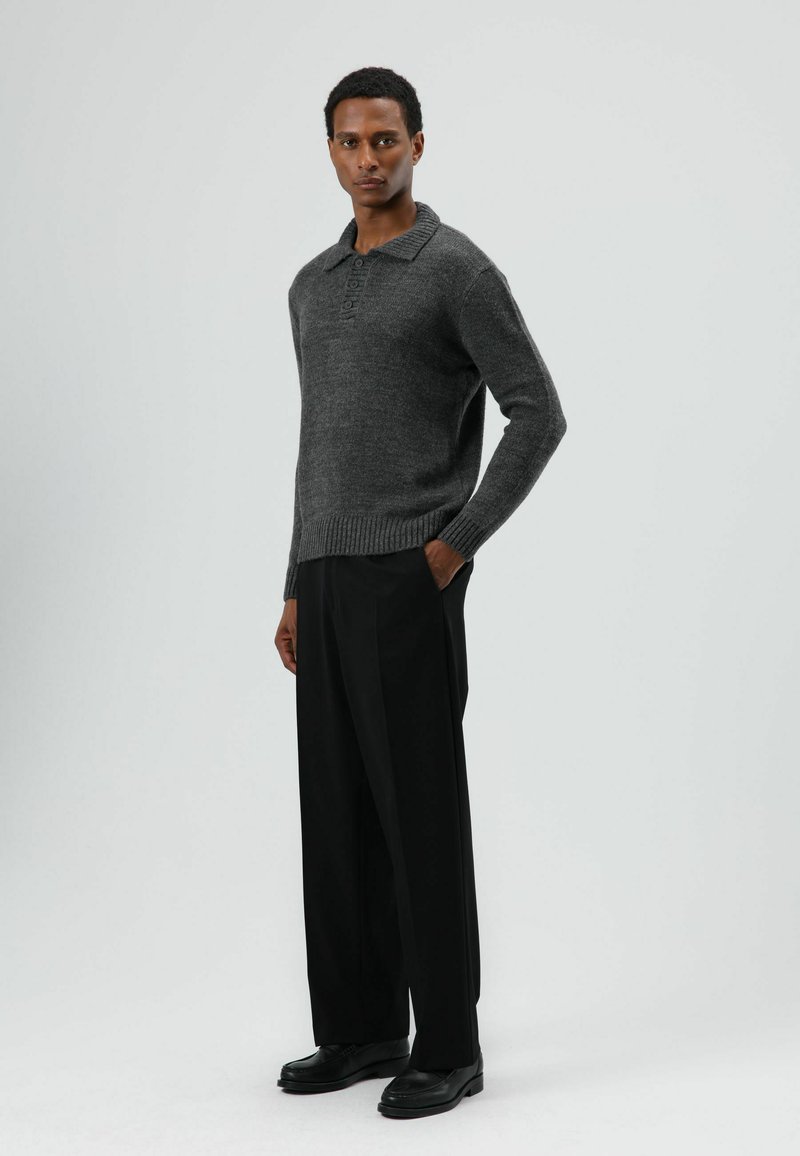 Grijze gebreide trui met kraag en knoopsluiting, gecombineerd met zwarte wijde broekspijpen en zwarte schoenen. Eenvoudig en gestructureerd ontwerp.