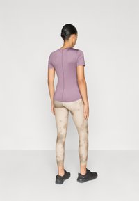 Μπλούζα λεβάντας με κοντά μανίκια συνδυασμένη με μπεζ κολάν με μοτίβο tie-dye και μαύρα αθλητικά παπούτσια, από την πίσω όψη.