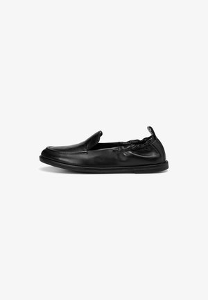Black leather slip-on shoe with a rounded toe, elasticized top edge, and a textured, flexible sole. Minimalistic design with no visible hardware.