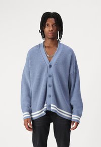 Ljusblå stickad cardigan med V-hals, sex knappar och vita randiga detaljer vid ärmsluten och kanten. Avslappnad passform, ribbad textur.