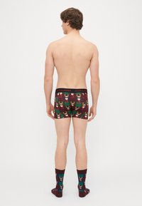 Boxers en plaid rouge et vert avec des motifs de rennes, dotés d'une ceinture noire affichant "JACK & JONES". Chaussettes foncées avec des rennes assortis.