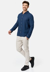 Camisa de botones de color navy con lunares blancos, combinada con pantalones beige y zapatillas negras. La camisa presenta un cuello clásico y mangas largas.