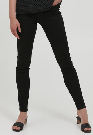 Black skinny jeans with a smooth texture and a snug fit, paired with black open-toe heeled mules, highlighting a minimalist design.